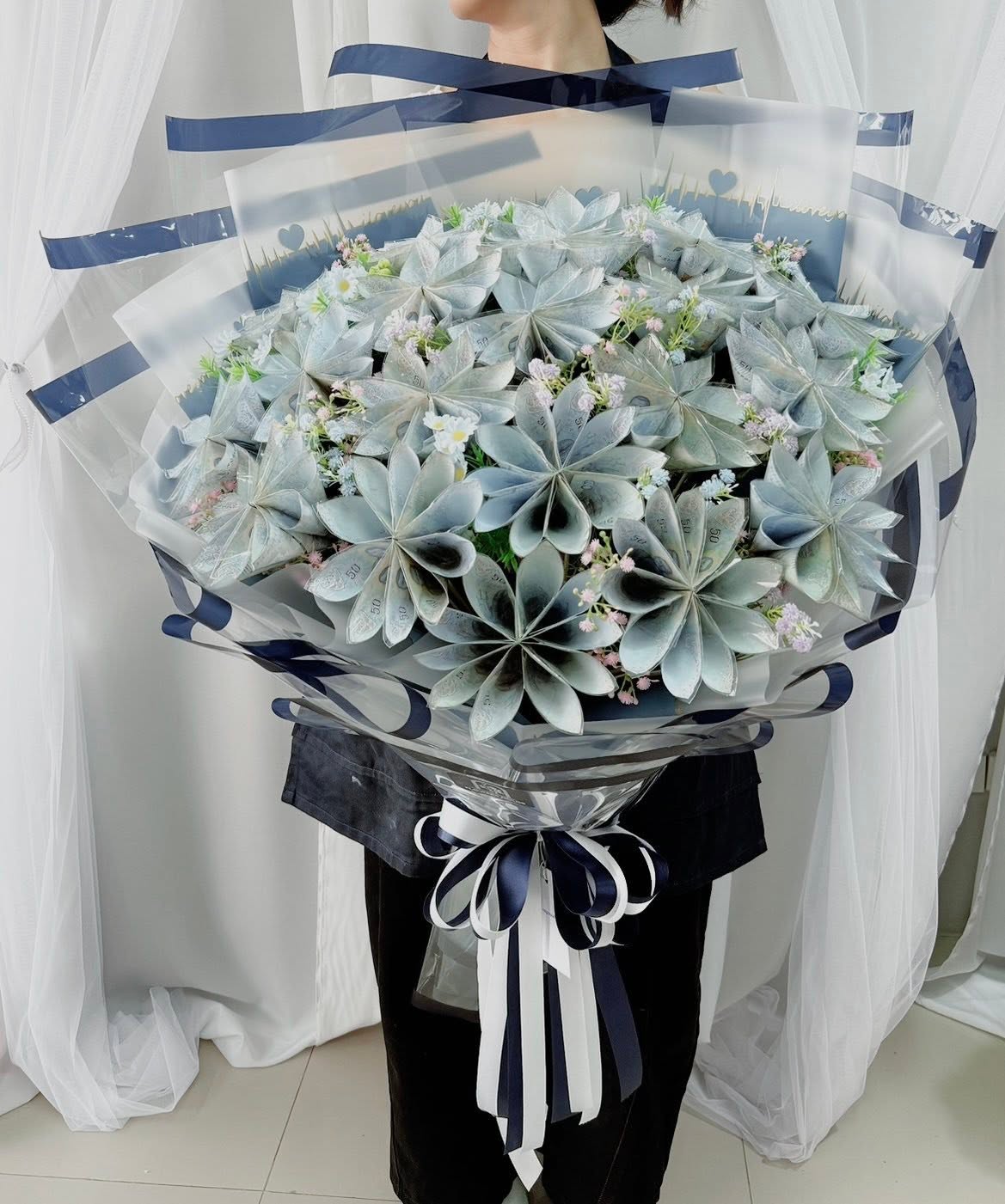 Money bouquet of folded banknotes with small flowers, wrapped in clear film and navy ribbon